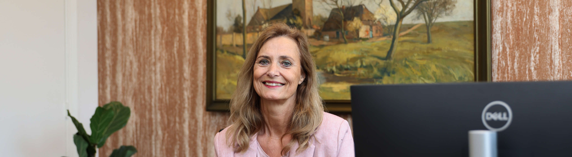 Jeanine lachend achter een bureau met beeldscherm.